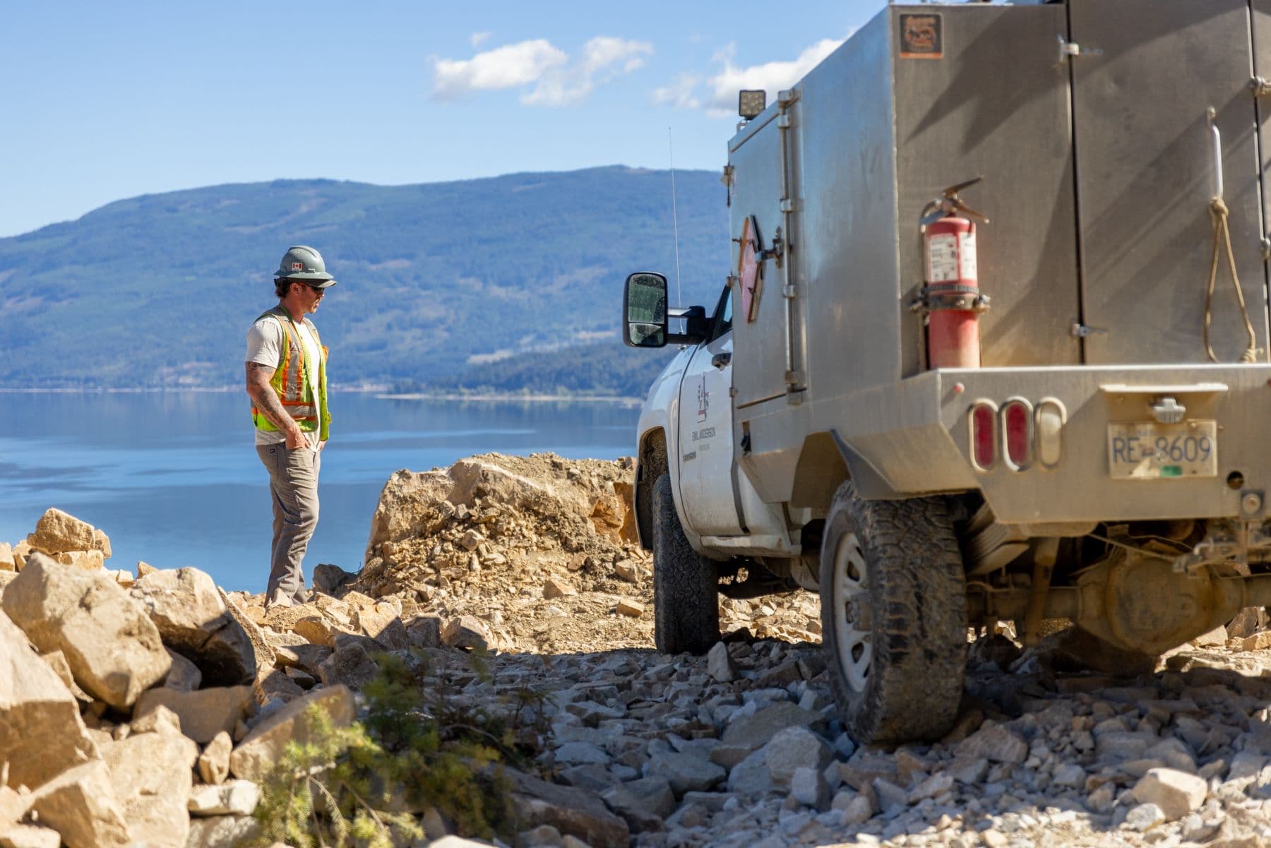 A construction worker standing next to a truck in a blasted rock area