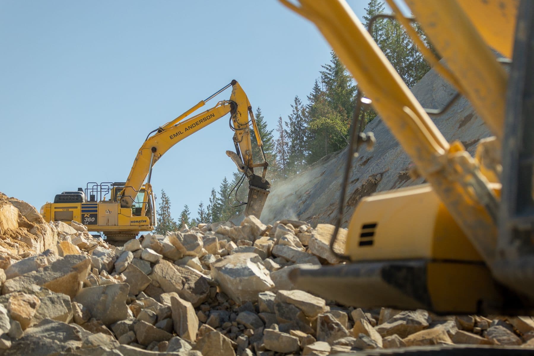 Two pieces of heavy equipment working at drilling rocks to clear the area