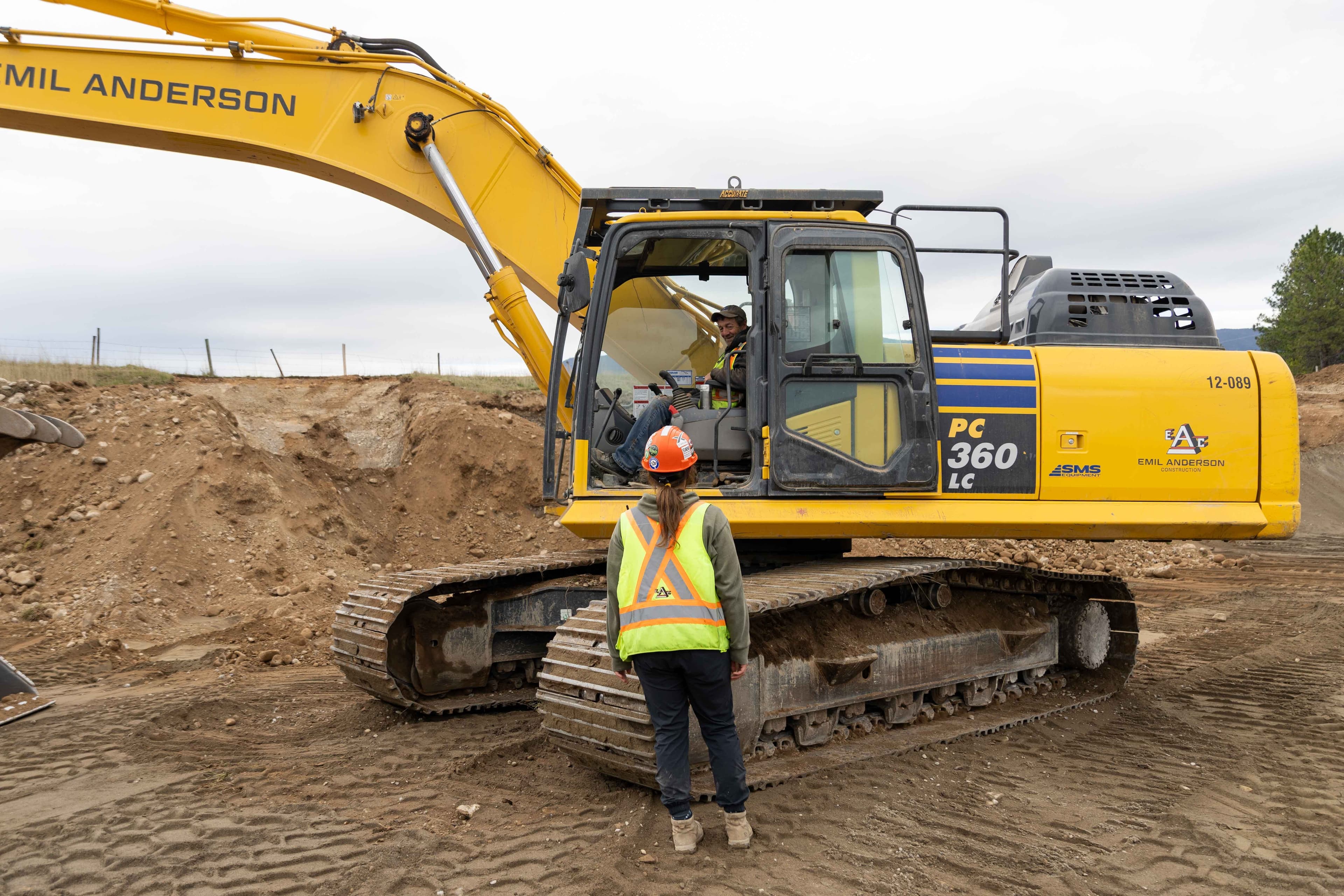 Two employees speaking. One is sitting in an excavator. 